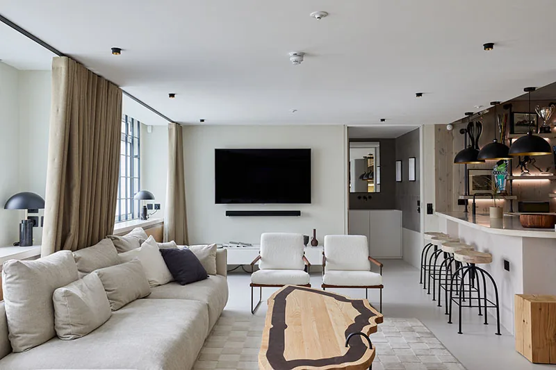 Living area with wall-mounted television, bespoke timber table and bar seating